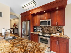 A modern kitchen with granite countertops, stainless steel appliances, and wooden cabinets. - Walk to Waves, Snorkeling, Golf & Restaurants (Lahaina)