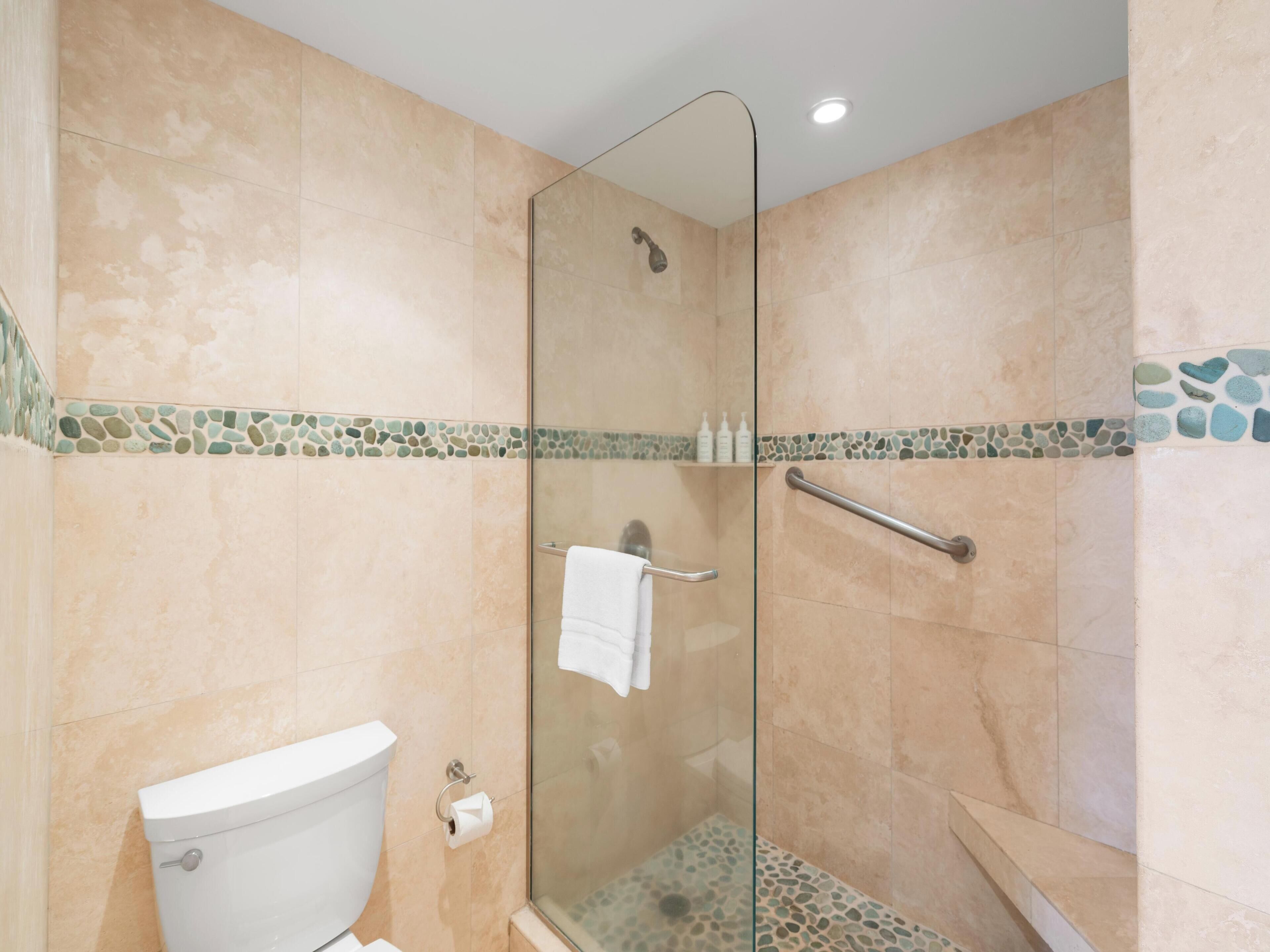 A modern bathroom with a glass-enclosed shower, beige tiles, and a glass shower door.
