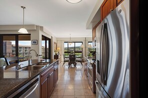 A modern kitchen with a large stainless steel refrigerator, a built-in dishwasher, and a dining area with a view. - Spacious Island Condo on Top-Voted Beach (Lahaina)