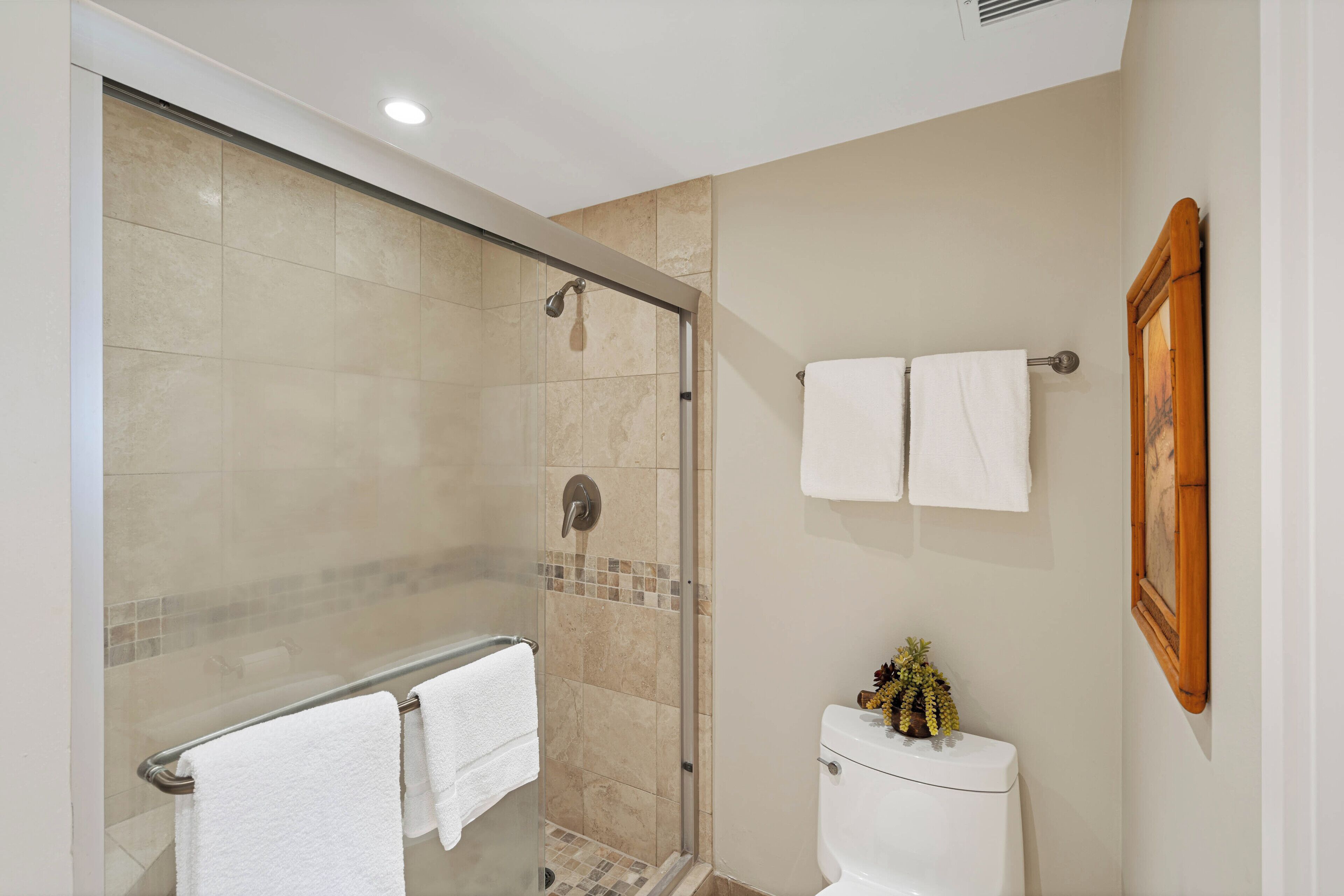 Un baño con ducha acristalada, inodoro y dos toallas blancas colgadas en un perchero.