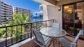 Ein Balkon mit Glastisch und Stühlen, mit Blick auf einen Strand und hohe Gebäude.