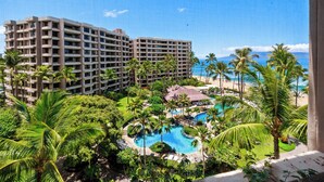 Ein Resort mit mehreren Gebäuden, einem von Palmen umgebenen Schwimmbad und einem Strand im Hintergrund.