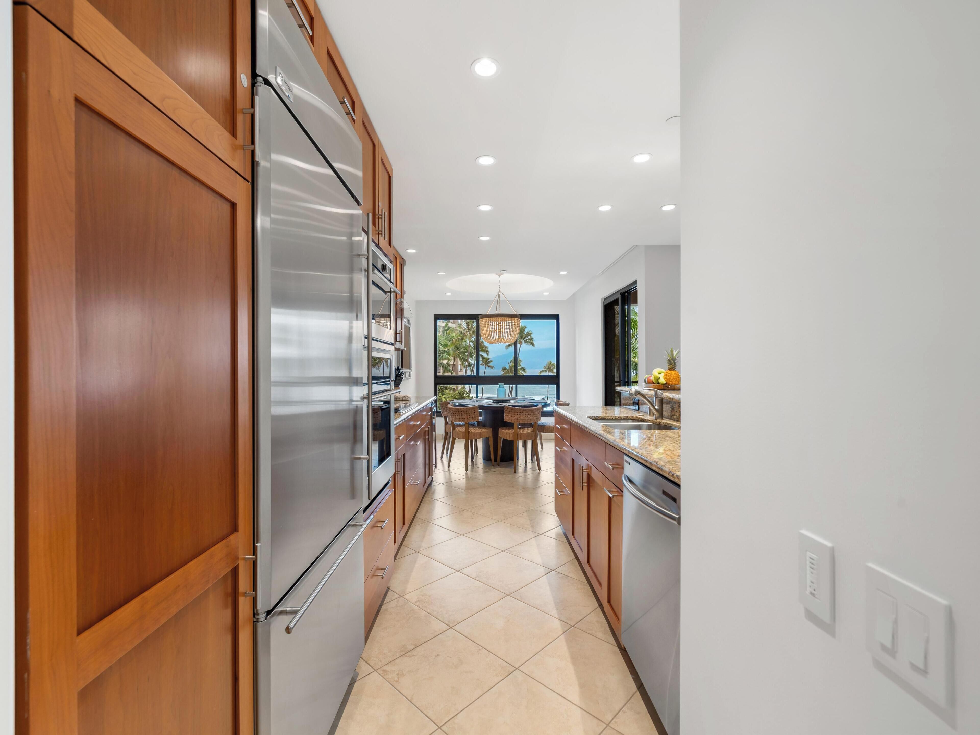 A modern kitchen with wooden cabinets, stainless steel appliances, and a view of the ocean through large windows.