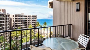 Un balcone con un tavolo in vetro e due sedie, con vista su una spiaggia e sullo skyline della città.