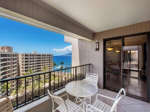 A balcony with a table and chairs, overlooking a beach and ocean. - Kaanapali Alii 1112 | Hot tub | Pool | Sunset Ocean Views (Lahaina)