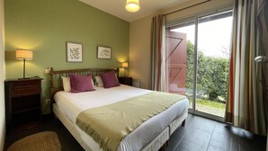 Een slaapkamer met een groot bed, twee bedlampen, een nachtkastje en uitzicht op groen door een schuifdeur.