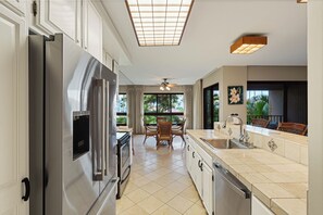 Eine moderne Küche mit Edelstahl-Kühlschrank, Backofen und Geschirrspüler. Ein Essbereich mit Tisch und Stühlen bietet einen Blick ins Freie durch große Fenster.