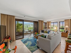 A spacious living room with a sofa, chairs, a coffee table, and a view of a landscape through large windows. - Sweeping Wrap-Around Tropical Views (Lahaina)