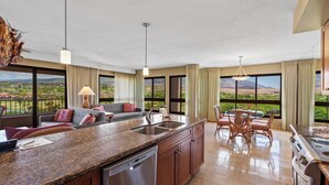 A spacious kitchen with granite countertops, a dishwasher, and a dining area with a table and chairs. - Golf Course & Mountain Views - Kaanapali Alii 2106 (Lahaina)