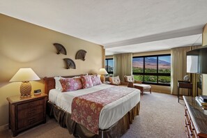 Ein Hotelzimmer mit einem großen Bett, zwei Nachttischen, einem Schreibtisch und einem Sessel. An den Wänden sind dekorative Ventilatoren angebracht und durch das Fenster ist eine Bergblick zu sehen.