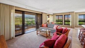 A spacious living room with a large sofa, a coffee table, and a view of a lush landscape through large windows. - Golf Course & Mountain Views - Kaanapali Alii 2106 (Lahaina)