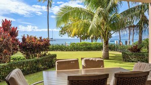 A covered outdoor seating area with a view of the ocean and palm trees. - Wraparound Oceanfront Views | Sleeps 8 | Resort Amenities Included (Lahaina)