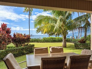 A covered outdoor seating area with a view of the ocean and palm trees. - Wraparound Oceanfront Views | Sleeps 8 | Resort Amenities Included (Lahaina)