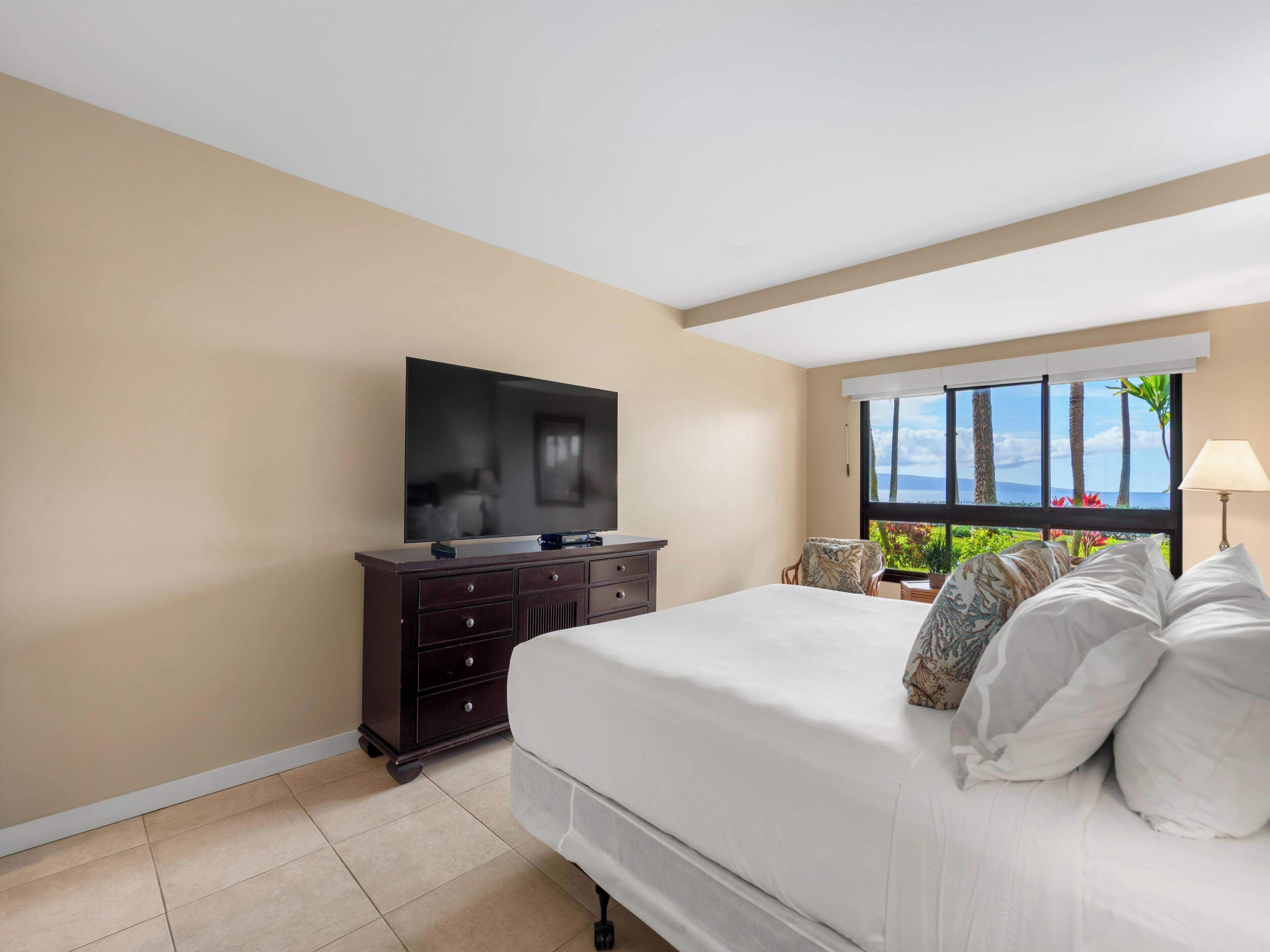 Habitación de hotel con cama, televisor en una cómoda, ventana con vista al mar y lámpara.