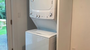 A compact, white laundry room with a built-in washer and dryer. It features a sliding door leading to a patio area with a wooden deck. - Renovated 3BR Home near  High Falls / Stone Ridge (Accord)
