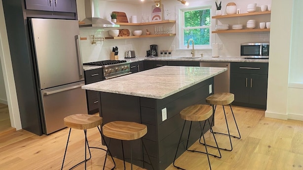 A modern kitchen with a central island, bar stools, a refrigerator, a stove, and wooden shelves above the counter. - Renovated 3BR Home near  High Falls / Stone Ridge (Accord)