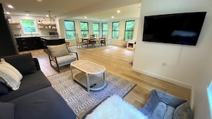 A modern living room with a sofa, armchair, and a coffee table. There is a TV mounted on the wall and a dining area in the background. - Renovated 3BR Home near  High Falls / Stone Ridge (Accord)