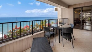 Un balcon avec vue sur l’océan, des meubles en osier et une porte vitrée donnant sur un espace intérieur.