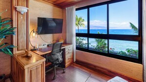 Ein Zimmer mit einem Holztisch, einem Sessel, einem Fernseher und einem großen Fenster mit Blick auf den Ozean.