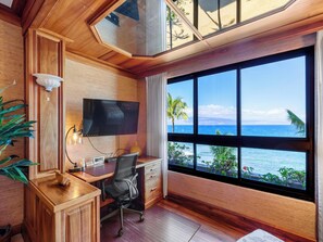 A room with a wooden desk, a chair, a TV, and a large window overlooking the ocean. - Sunsets, Sea Breezes & Oceanfront Living | Sleeps 6 w/ Resort Amenities (Lahaina)