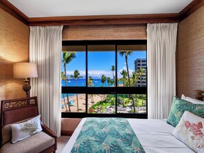 A hotel room with a large window offering a view of a beach and palm trees. - Sunsets, Sea Breezes & Oceanfront Living | Sleeps 6 w/ Resort Amenities (Lahaina)