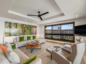 A modern living room with a large window, a ceiling fan, and a flat-screen TV. - Front-Row to the Pacific | Oceanfront Living at Kaanapali Alii (Lahaina)