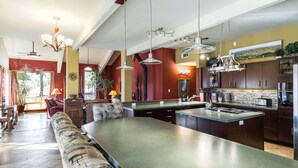Une cuisine spacieuse dotée d’un grand îlot central, d’un éclairage moderne suspendu et offrant une vue sur l’extérieur.