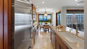 Una cocina moderna con un refrigerador de acero inoxidable, armarios de madera y un amplio ventanal con vista al océano.