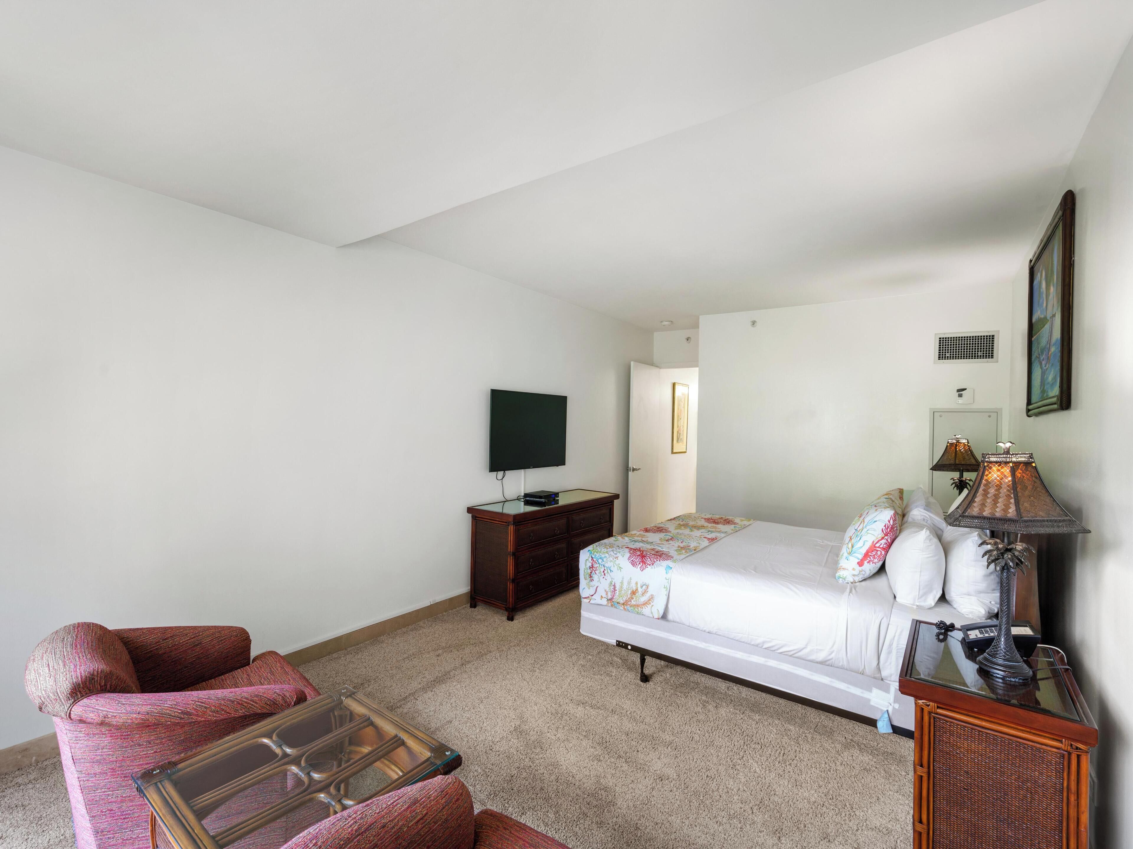 Un dormitorio con cama, televisor, cómoda y una silla.