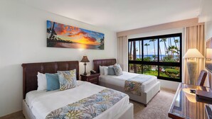 Una habitación de hotel con dos camas, un ventanal con vistas a palmeras y al atardecer, y un escritorio con una lámpara.