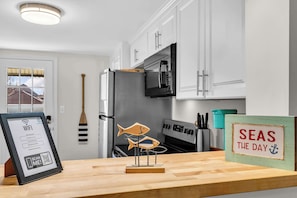 Eine Küche mit weißen Schränken, einer Mikrowelle, einem Kühlschrank und einer Holzdruck-Fischdekoration auf der Arbeitsfläche.