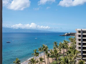 A coastal view with a beach, palm trees, and a building with balconies. - Kaanapali Beach Ocean Views | Great for Families (Lahaina)