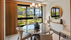 Een moderne eethoek met een glazen tafel, witte stoelen en uitzicht op palmbomen en de oceaan.