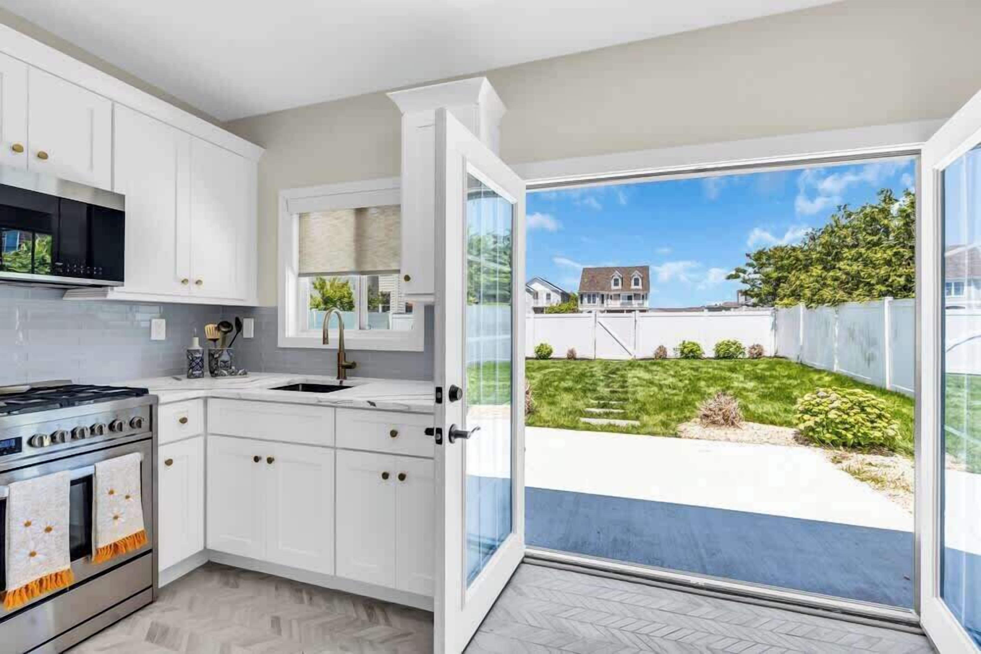 A modern kitchen with white cabinets, a stainless steel stove, and a large window opening to a backyard.