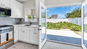 Een moderne keuken met witte kastjes, een roestvrijstalen fornuis en een groot raam dat uitkijkt op een achtertuin.