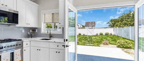 Een moderne keuken met witte kastjes, een roestvrijstalen fornuis en een groot raam dat uitkijkt op een achtertuin.