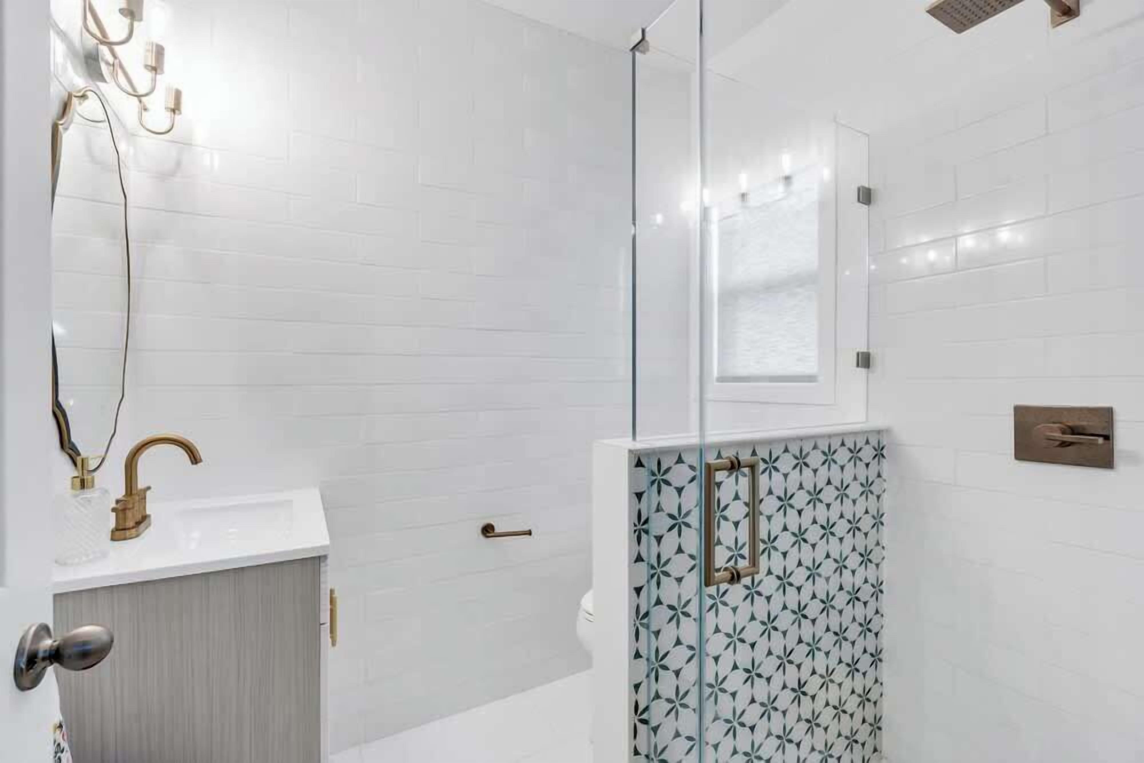 Une salle de bain moderne avec des carreaux de céramique blancs rectangulaires, une douche en verre, un robinet doré et un meuble en bois.