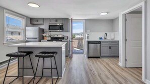 A modern kitchen with a central island, bar stools, and a view to a balcony. - Wildwood Waves - 2BR Apt - Steps from Beach (Wildwood)
