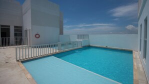 En swimmingpool med ett vitt staket och en livboj, omgiven av en byggnad med stora fönster.