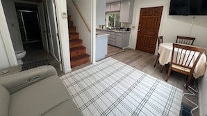 Ein Wohnzimmer mit einer Couch, einem karierten Teppich, einem Esstisch mit Stühlen, einer Küchenzeile und einer Treppe.