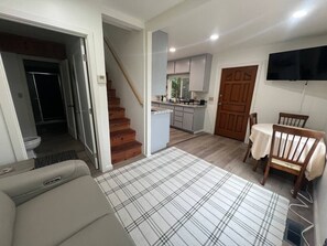 A living room with a sofa, a plaid rug, a dining table with chairs, a kitchen area, and a staircase. - Baker Beach Seagull House Trinidad Harbor Views (Trinidad)