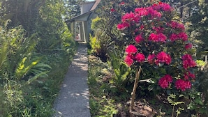 Ein Gartenweg führt zu einem Haus, umgeben von üppigem Grün und blühenden Pflanzen.