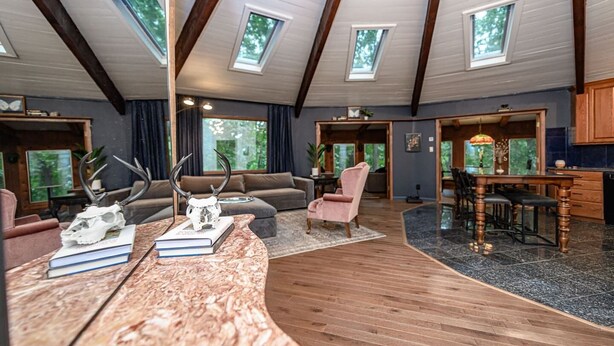 A spacious living area with a high ceiling, skylights, a fireplace, and a dining area.