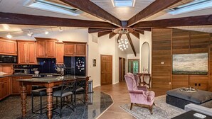 A spacious kitchen with wooden cabinets, a central island, and a dining area with a pink chair.