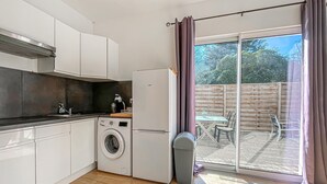 Een kleine keuken met een wasmachine, een koelkast en een eethoek met een tafel en stoelen.