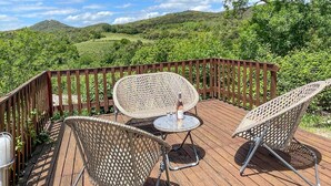 A wooden deck with wicker chairs and a table, overlooking a lush green landscape.