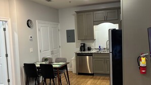 A modern kitchen with stainless steel appliances, a dining area with a wooden table and chairs, and a fire extinguisher mounted on the wall.