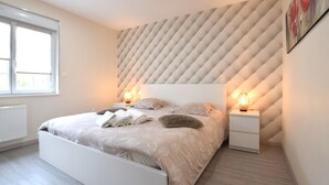 A modern bedroom with a large bed, two bedside tables, and a geometric patterned wall. - Maison cosy proche mer (Créances)