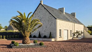 A stone building with a sloped roof, a star on the wall, and a palm tree in the foreground. - Maison cosy proche mer (Créances)