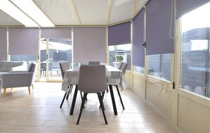 A sunroom with a dining table and chairs, large windows, and a view of the outside. - Maison cosy proche mer (Créances)